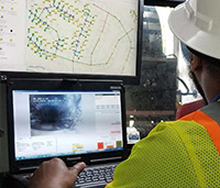 Man in hard hat looking at utility map on computer