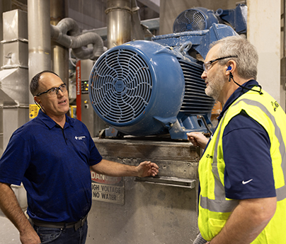 Two men in PPE are talking while they stand next to a piece of equipment at Clearwater Paper.