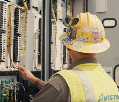 Worker wearing hard hat and safety vest looks at substation breakers